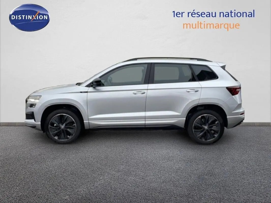 Profil droit d’un Skoda Karoq argent 2025 avec barres de toit et jantes noires sportline.
