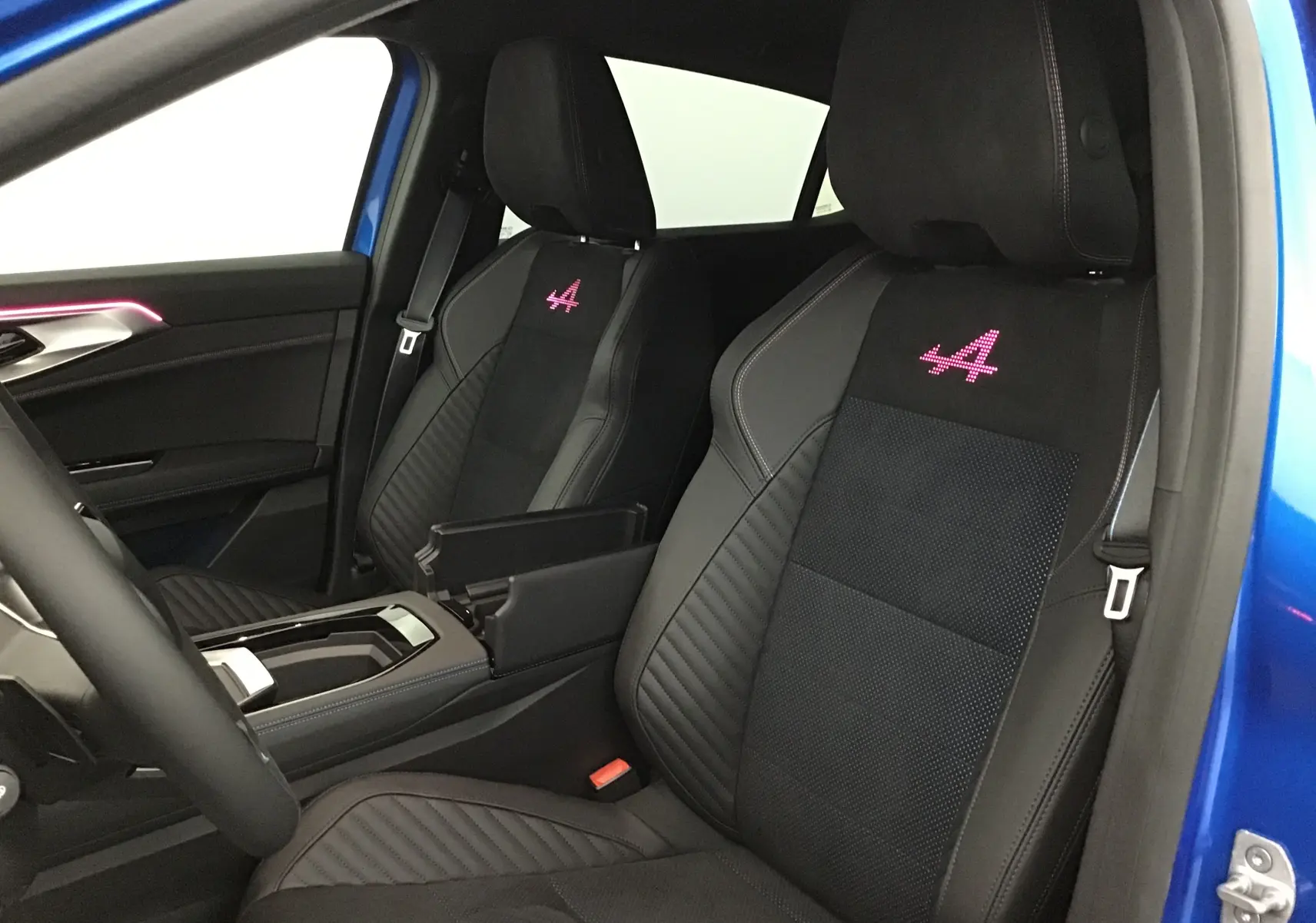 Vue intérieure côté conducteur du Renault Rafale 2025 bleu sommet, sièges Alcantara noirs avec logo Alpine rose brodé.