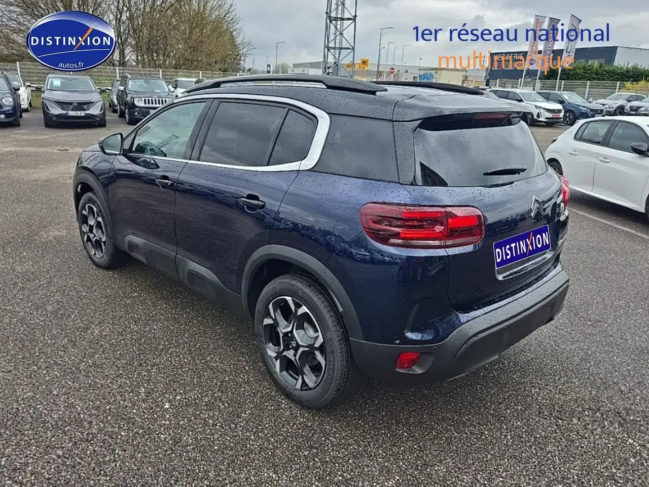 Vue 3/4 arrière droite d'un Citroën C5 Aircross bleu eclipse avec toit noir et jantes alu 18 pouces sur parking.