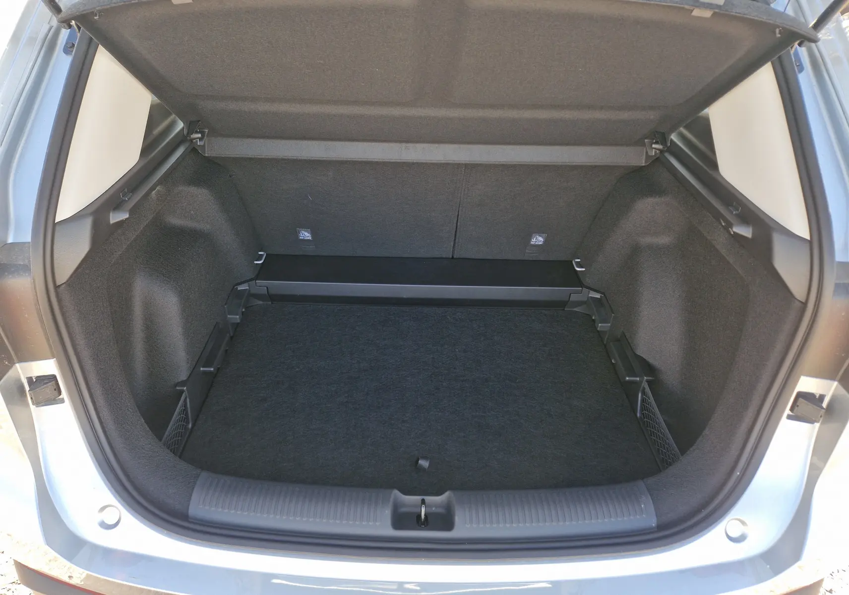 Coffre ouvert vu de l'arrière d'un MG MOTOR 1.5 L Hybrid+ Cosmic Silver, intérieur noir et compartiments latéraux.