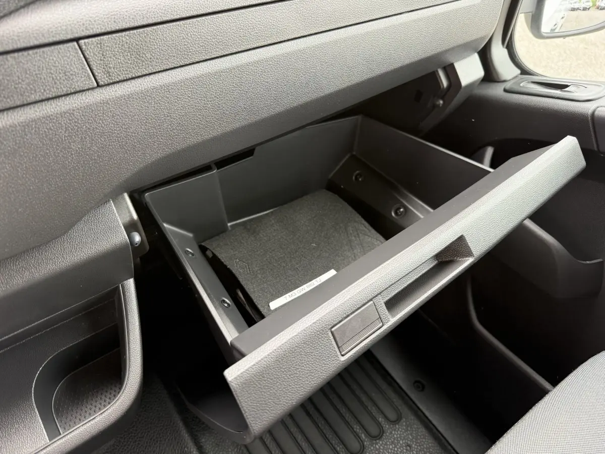 Vue rapprochée de la boîte à gants ouverte côté passager dans l’habitacle noir du Renault Master blanc 2024.