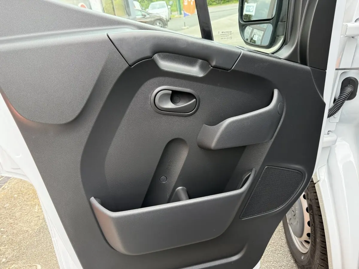 Vue rapprochée de la porte côté conducteur du Renault Master blanc, avec poignée intérieure et haut-parleur intégré.