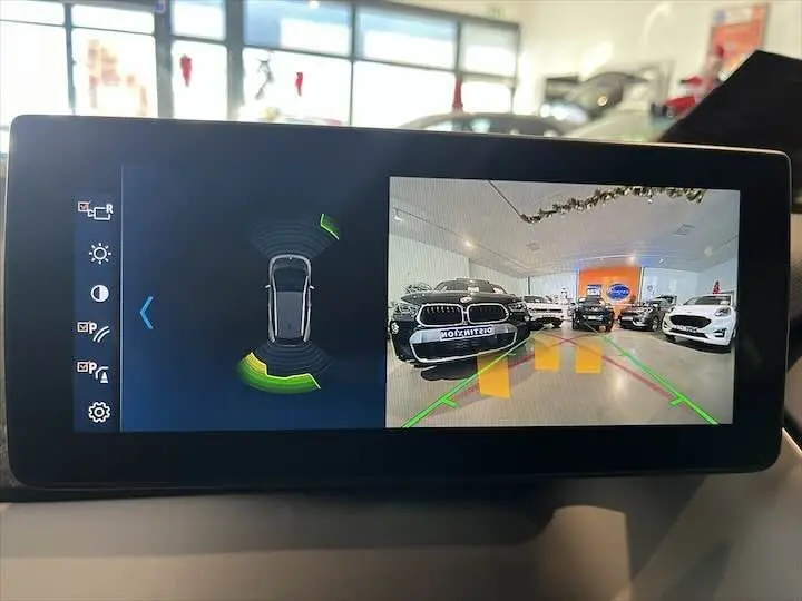 Écran de caméra de recul montrant plusieurs véhicules en showroom, dont une BMW noire en 3/4 avant face caméra.