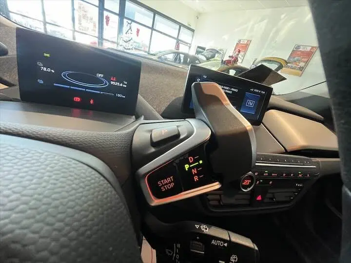 Détail du tableau de bord et levier de vitesses de la BMW i3 noire, avec affichage numérique et commandes au volant visibles.