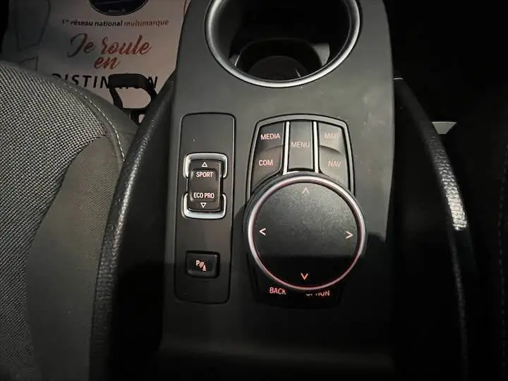 Gros plan sur la molette de commande multimédia et les boutons de mode de conduite dans l'habitacle gris-bleu d'une BMW i3 noire.