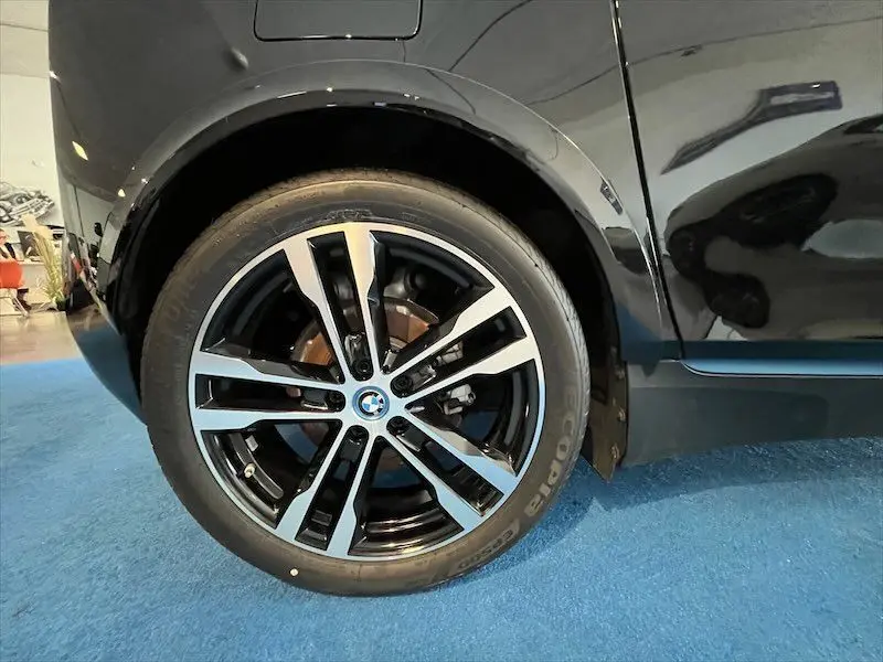 Gros plan sur la roue arrière gauche noire brillante d'une BMW i3 Edition Windmill avec jante bi-ton moderne.