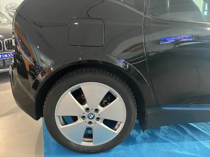 Gros plan sur la roue arrière gauche d'une BMW i3 noire, mettant en valeur la jante spécifique et la trappe de recharge électrique.