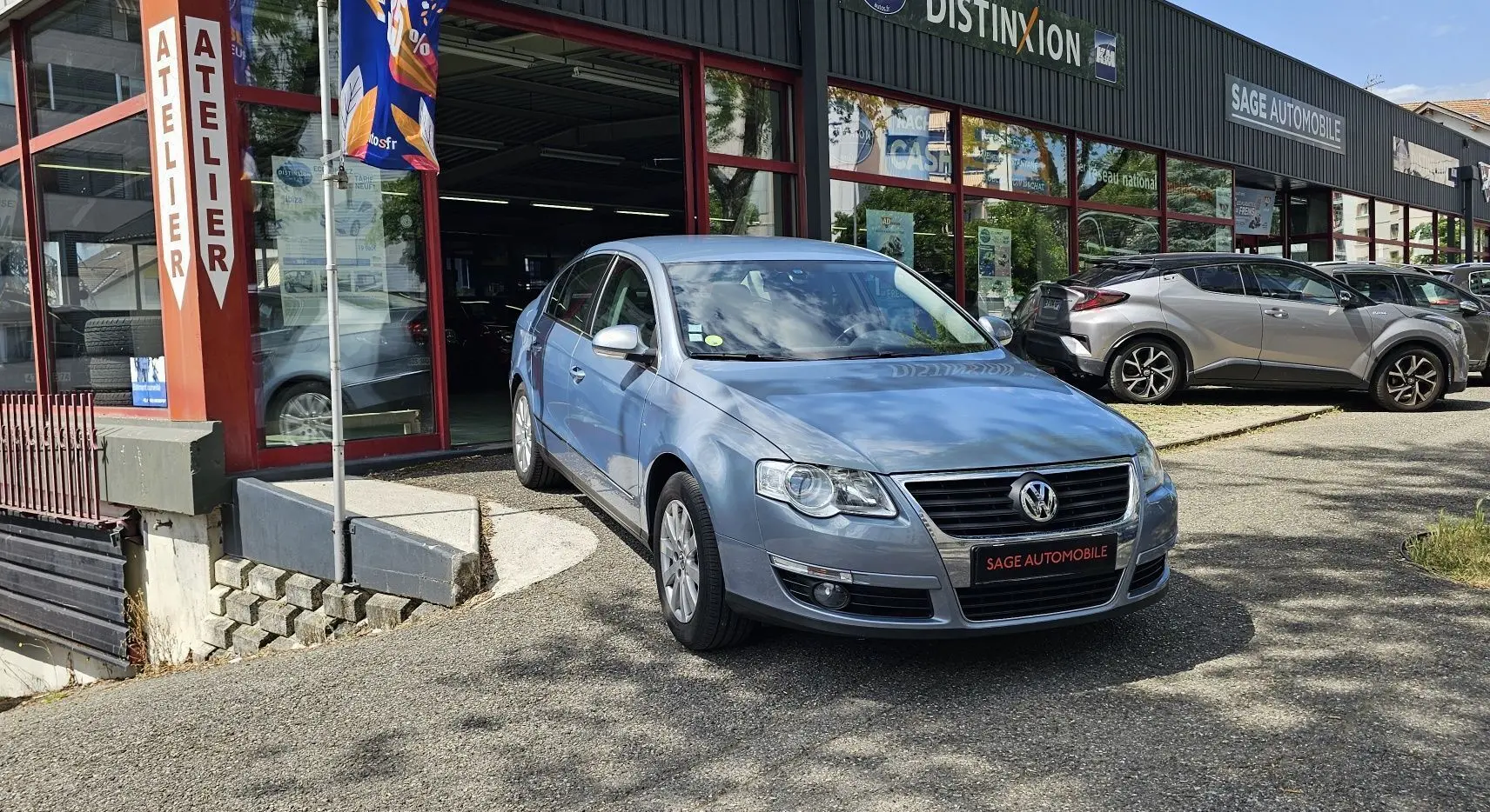 Volkswagen Passat 1.4 TSI bleu vue 3/4 avant droit devant un garage avec plaque Sage Automobile.