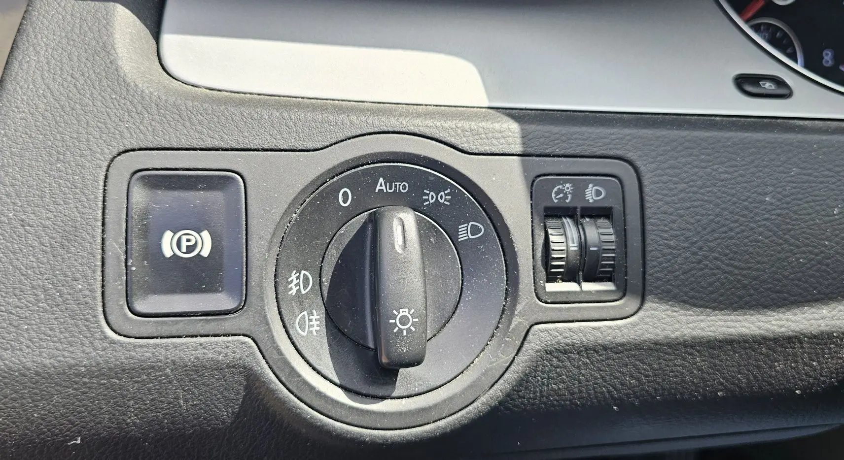 Gros plan sur le bouton de commande des phares et frein à main électrique dans une Volkswagen Passat bleu 2009.