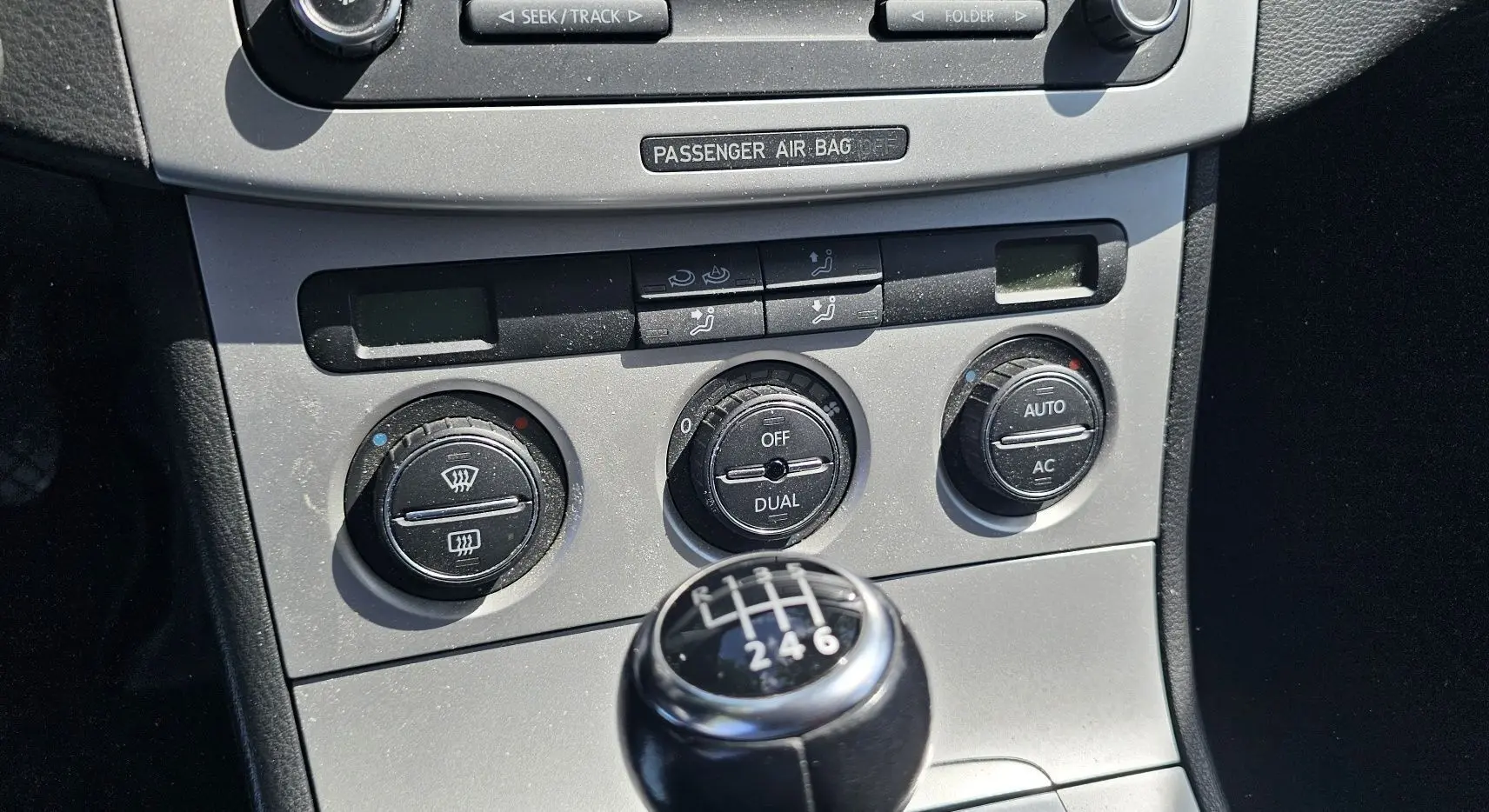 Gros plan sur la console centrale de la Volkswagen Passat 2009, mettant en valeur la commande de climatisation et le levier de vitesse manuel noir.