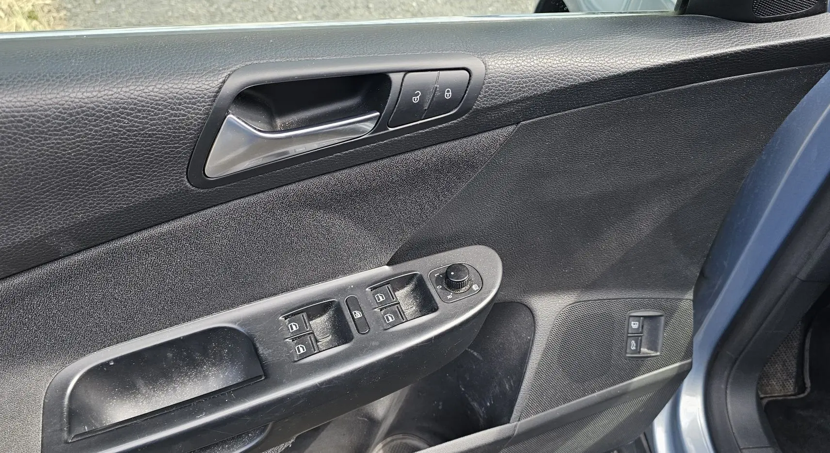 Vue rapprochée de la portière avant gauche bleue d'une Volkswagen Passat 2009, avec commandes électriques et poignée chrome.