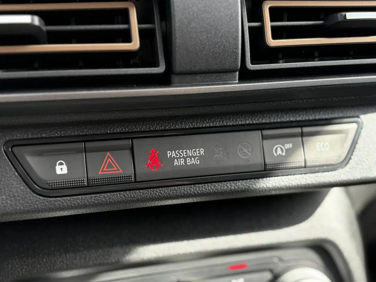 Gros plan sur la rangée de boutons du tableau de bord du Dacia Jogger gris, avec témoin airbag passager rouge allumé.