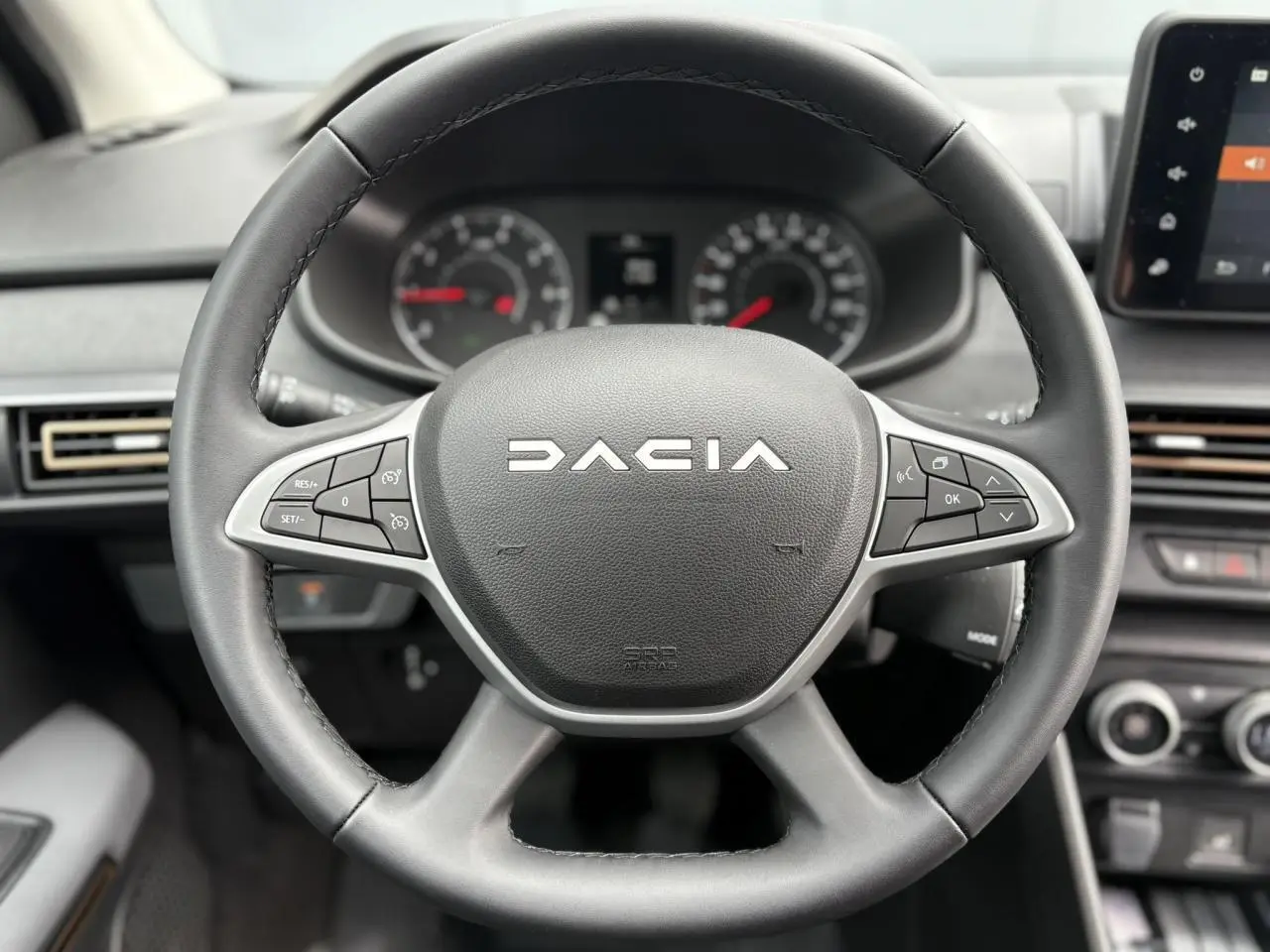 Gros plan sur le volant noir du Dacia Jogger 2025 avec commandes intégrées et tableau de bord flou en arrière-plan.