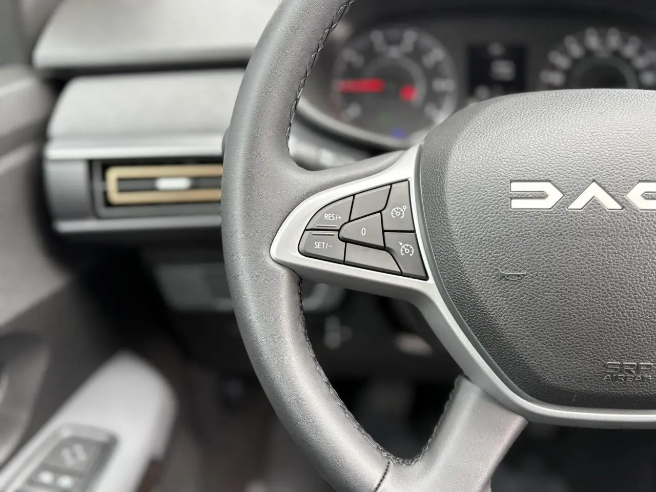 Gros plan sur le volant noir du Dacia Jogger 2025 avec commandes de régulateur de vitesse et tableau de bord flou.