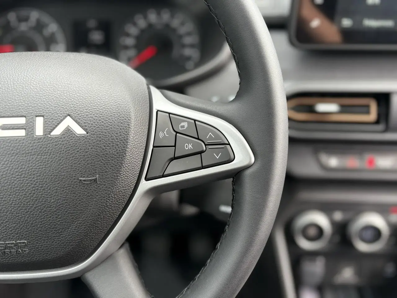 Gros plan sur le volant noir de la Dacia Jogger 2025 avec commandes multifonctions et tableau de bord flou en arrière-plan.