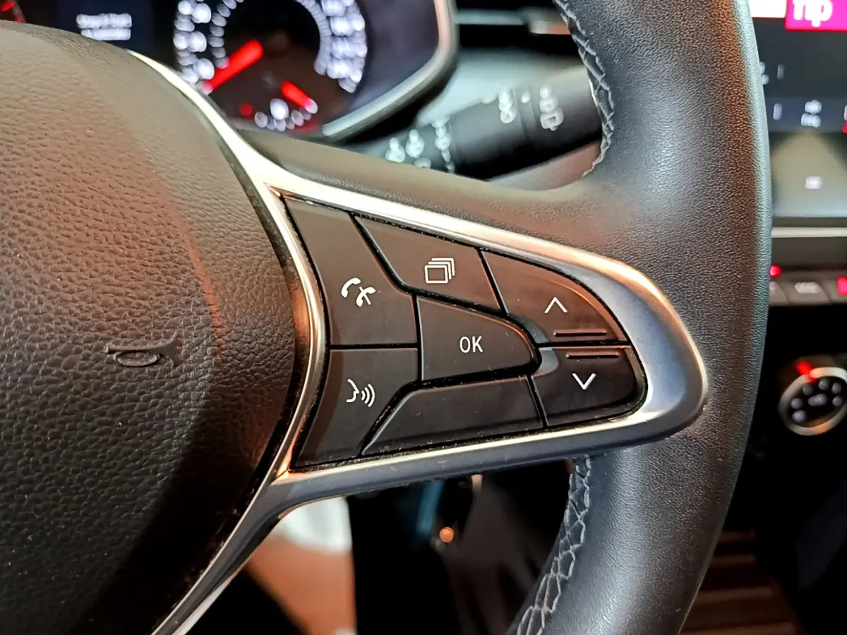 Gros plan sur le côté droit du volant en cuir noir de la Renault Clio Business blanc, avec commandes multifonctions visibles.