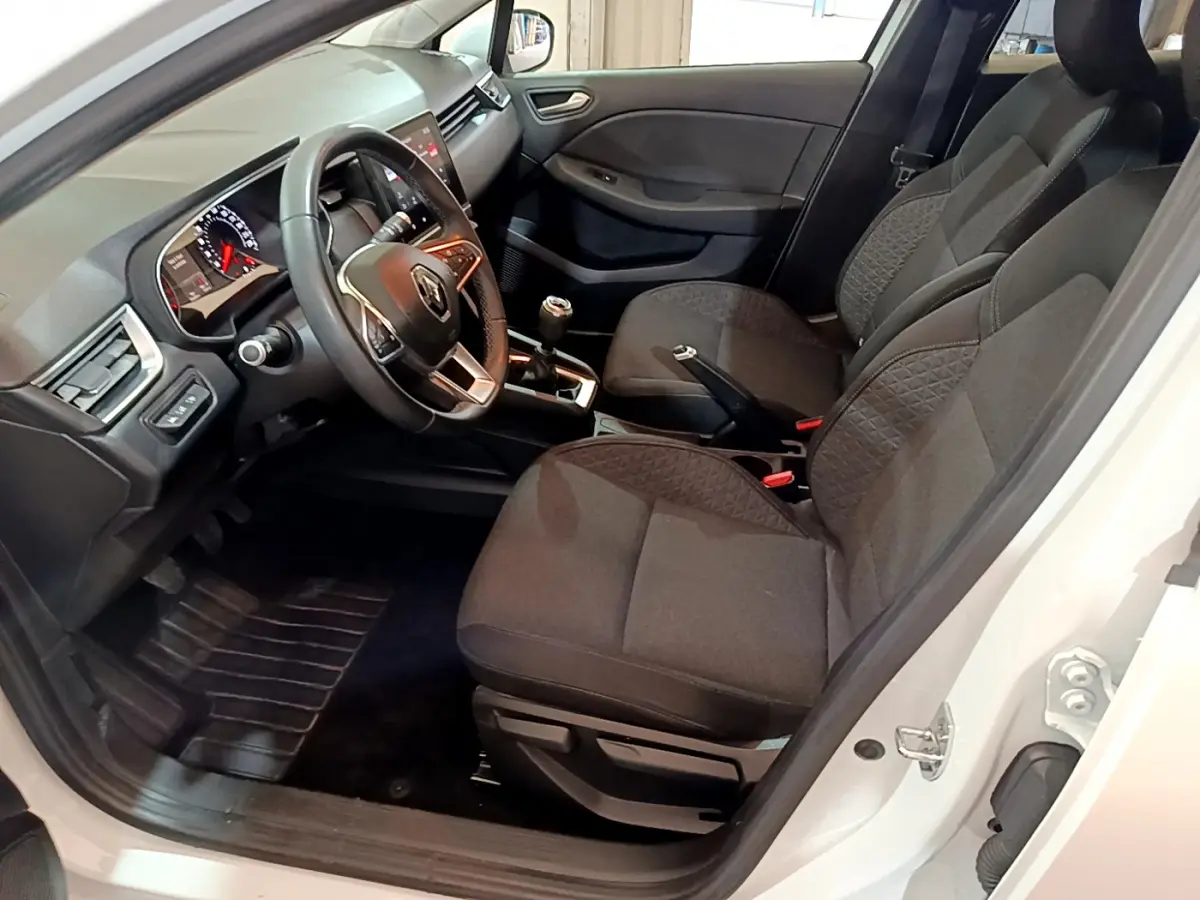 Intérieur côté conducteur d'une Renault Clio blanche 2020, sièges noirs, volant cuir et levier de vitesse manuel visibles.