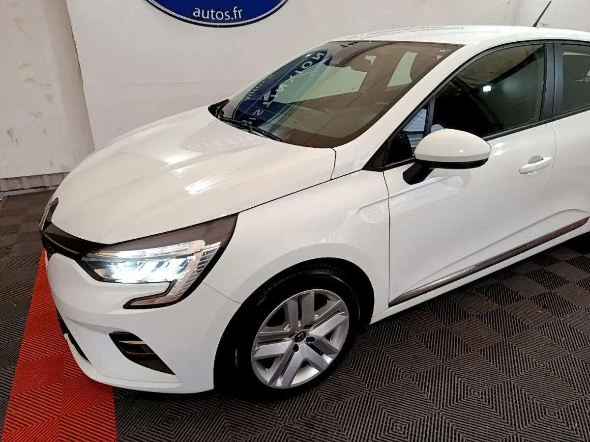 Vue 3/4 avant droit d'une Renault Clio Business Blue dCi 85 blanche avec phares LED allumés et jantes alliage.