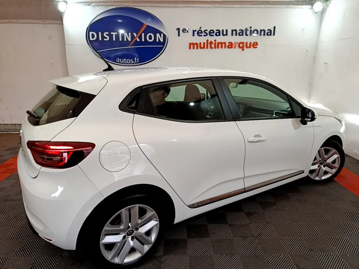 Vue de profil côté gauche d'une Renault Clio Business Blue dCi 85 blanche avec jantes alliage et feux arrière allumés.