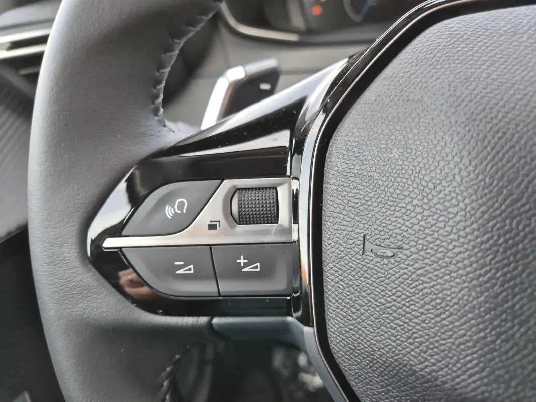Gros plan sur les commandes gauche du volant noir de la Peugeot 208 Hybrid 110 e-DCS6 Allure blanche de 2025.