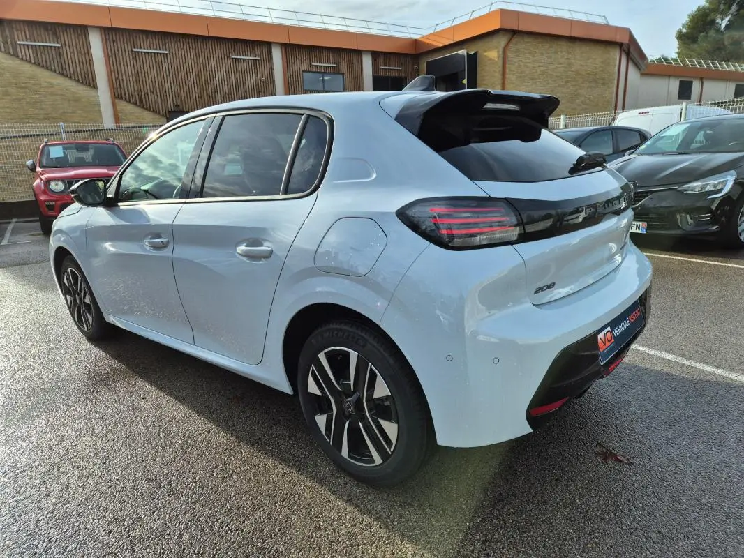 Vue 3/4 arrière droite d'une Peugeot 208 blanche 2025 avec jantes alliage noires et feux arrière LED distinctifs.