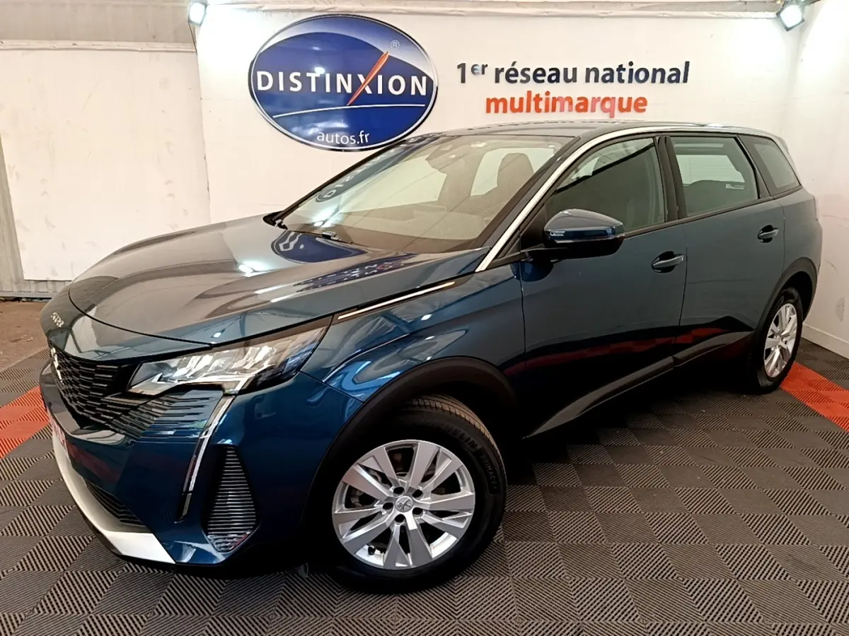 Peugeot 5008 bleu en 3/4 avant droit, avec calandre noire et jantes argentées, dans un showroom intérieur.