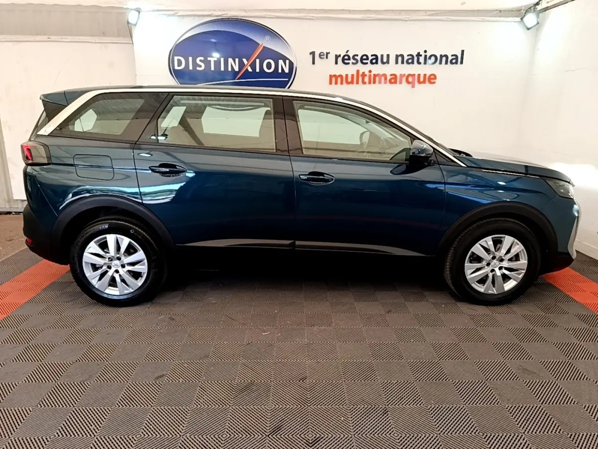 Vue de profil côté gauche d’un Peugeot 5008 bleu 2021 garé en intérieur avec jantes argentées et toit noir.