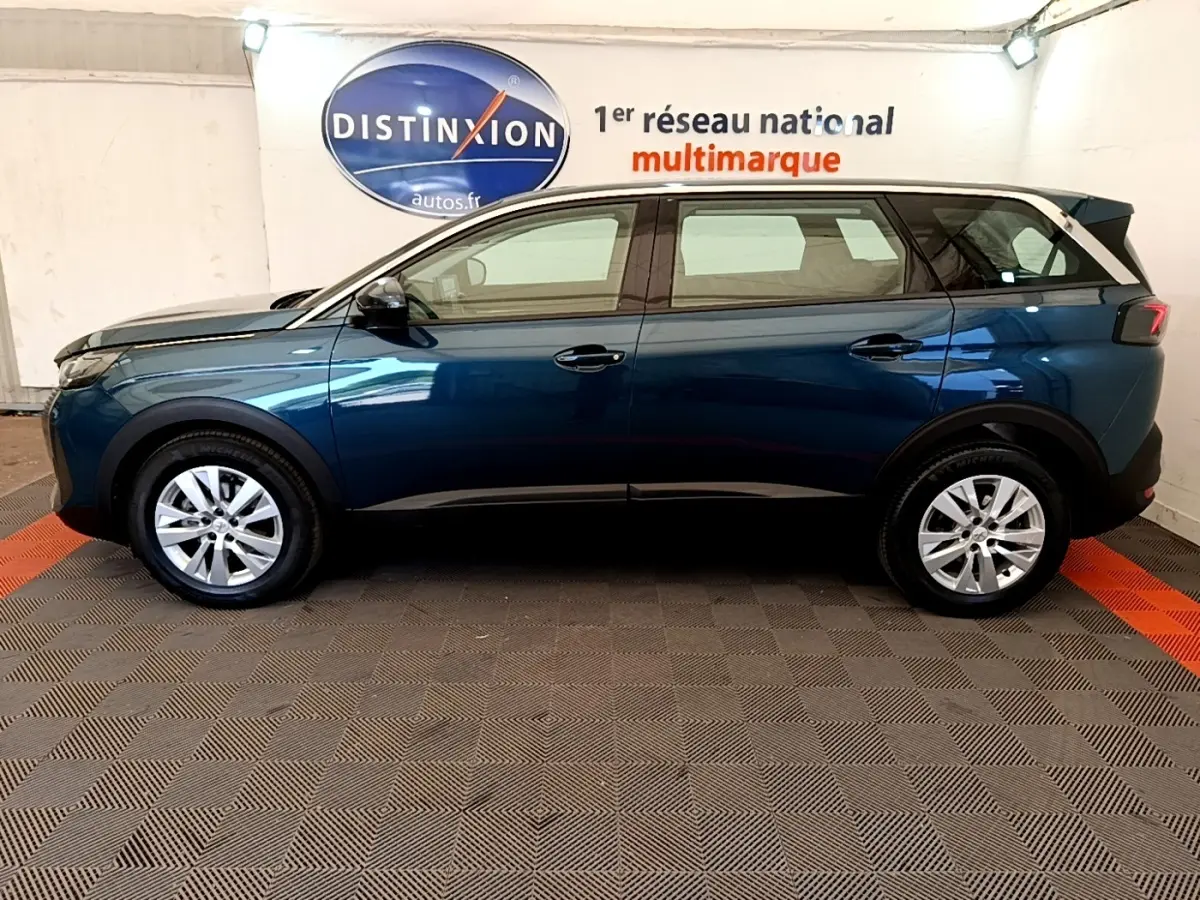 Vue de profil côté gauche d'un Peugeot 5008 bleu 2021 stationné en intérieur avec jantes alliage et vitres teintées.