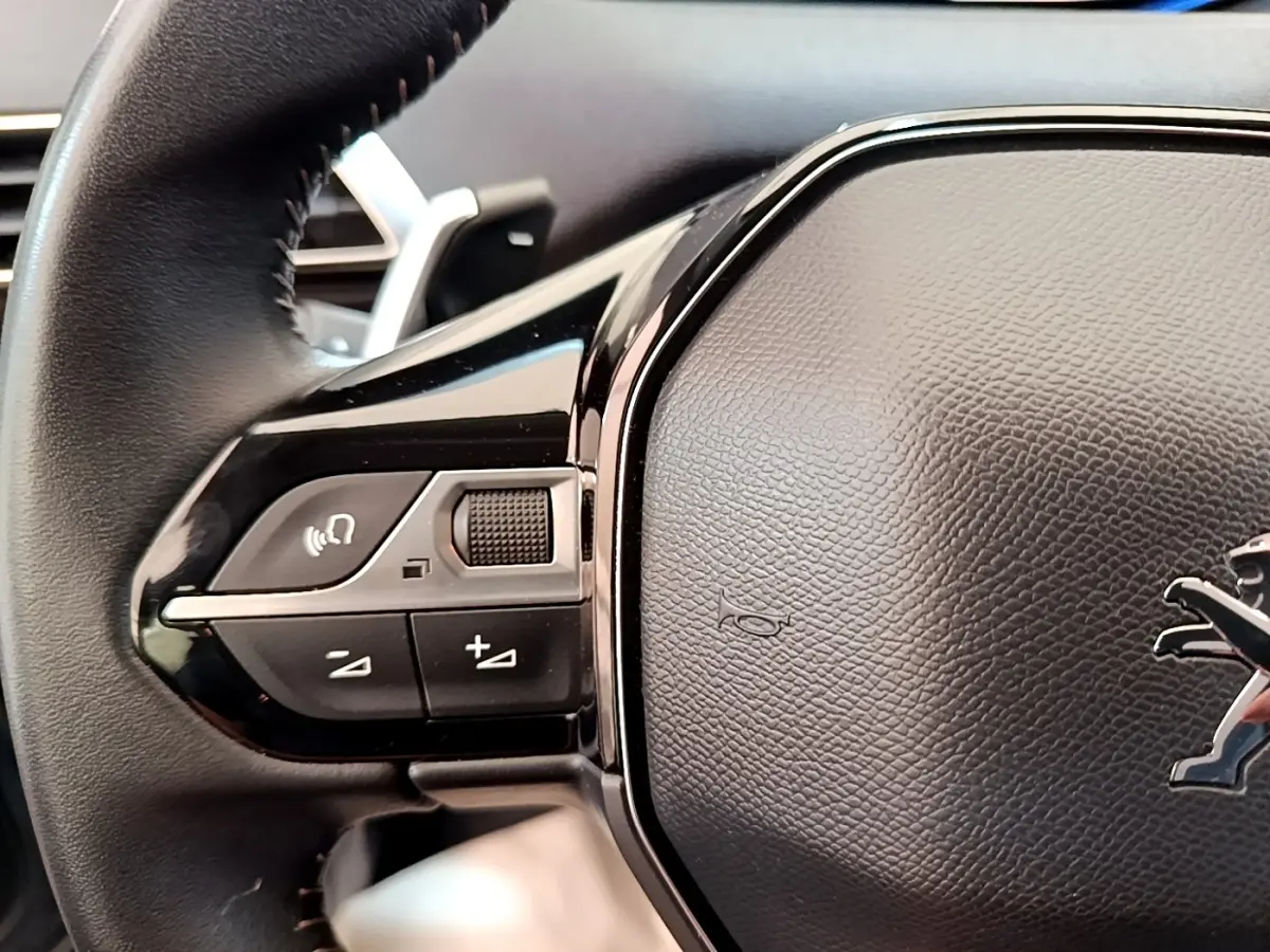 Gros plan sur le volant cuir noir multifonctions du Peugeot 5008 avec commandes audio et logo lion central.