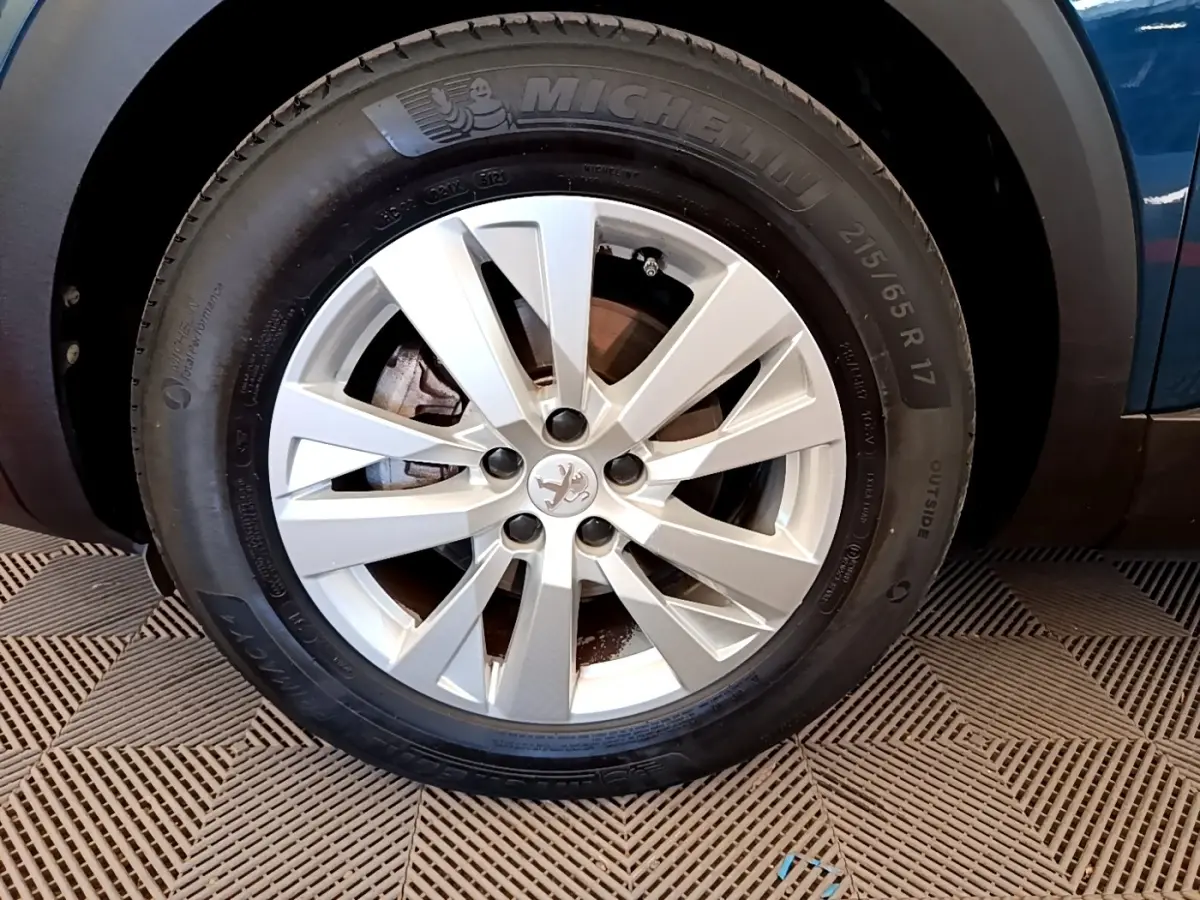 Gros plan sur la roue avant droite d’un Peugeot 5008 bleu, avec jante alliage argentée et pneu Michelin.