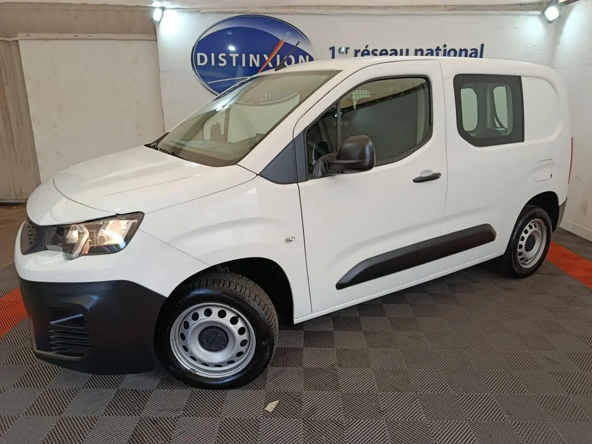 Vue 3/4 avant droit d’un utilitaire Peugeot Partner blanc avec jantes acier et protections noires sur les portes.