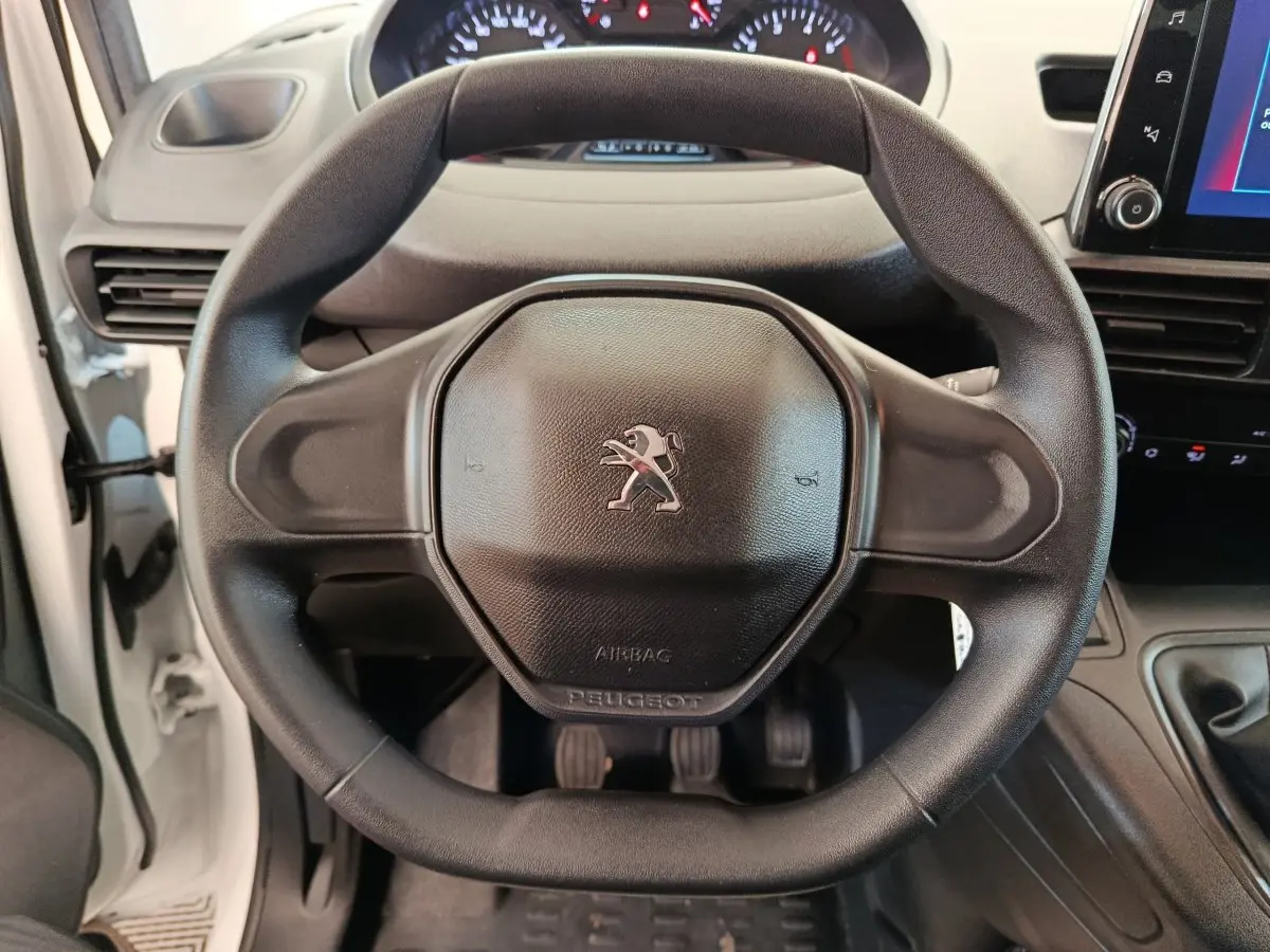 Vue rapprochée du volant noir du Peugeot Partner blanc 2021, avec tableau de bord et levier de vitesse visibles.