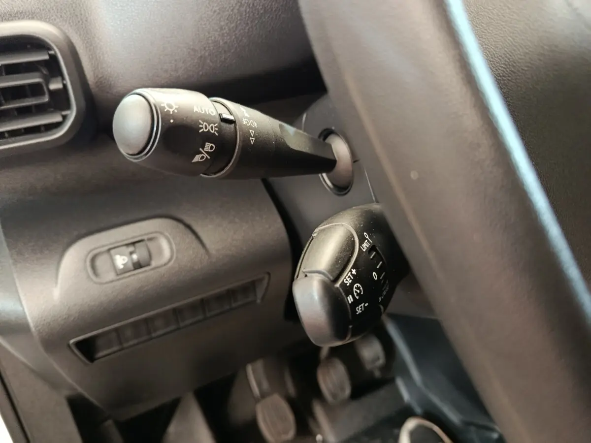 Gros plan sur les commandes de phares et régulateur de vitesse du Peugeot Partner blanc, vue côté conducteur intérieur.