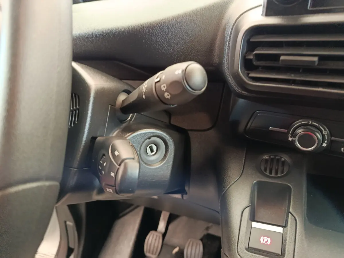Gros plan sur la colonne de direction et la commande de frein à main électrique dans l'habitacle noir du Peugeot Partner blanc.