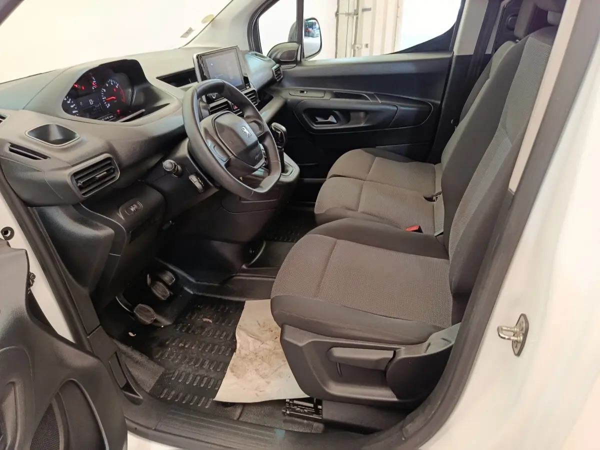 Vue intérieure côté conducteur du Peugeot Partner blanc 2021, montrant le tableau de bord et les sièges avant en tissu gris.