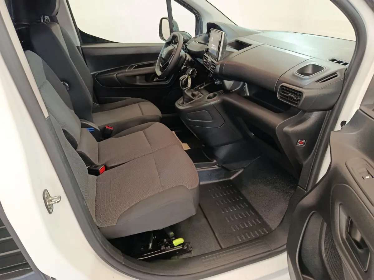 Vue intérieure côté conducteur du Peugeot Partner blanc 2021, montrant les sièges avant et le tableau de bord noir.