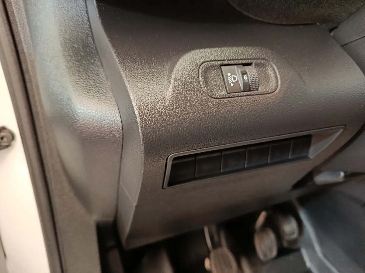 Détail intérieur côté gauche du tableau de bord noir avec commande de réglage des phares du Peugeot Partner blanc.