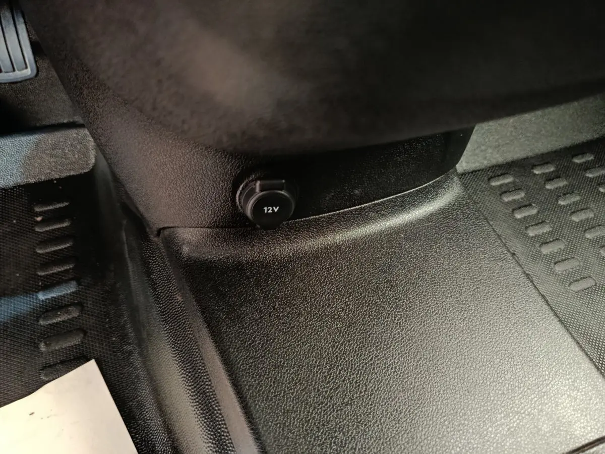 Prise 12V noire sur la console centrale, plancher et tapis en caoutchouc noir du Peugeot Partner blanc 2021.