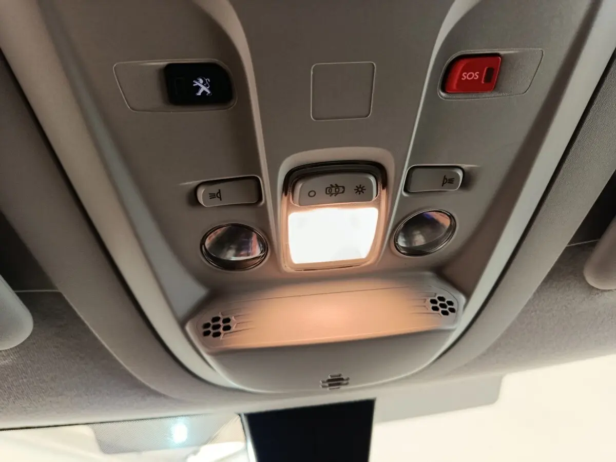 Plafonnier intérieur avec éclairage, boutons de commande et bouton SOS du Peugeot Partner blanc, vue en contre-plongée.