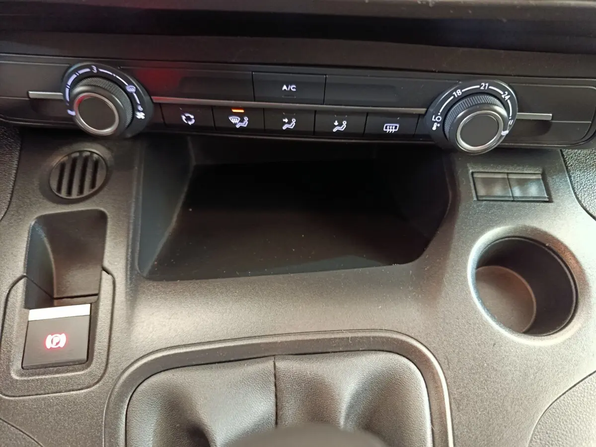 Vue rapprochée de la console centrale noire du Peugeot Partner 2021, avec commandes climatisation et frein à main électrique.