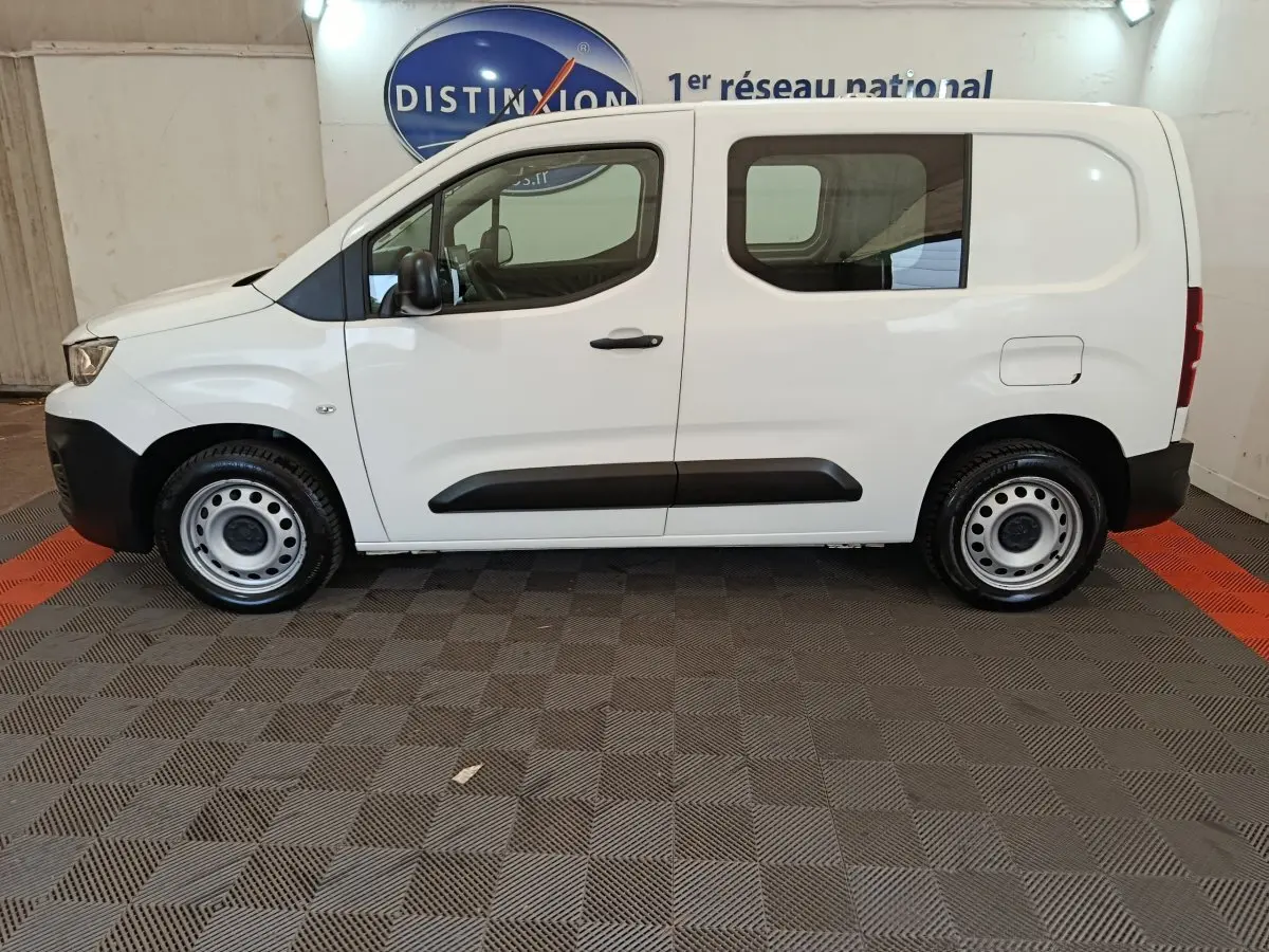 Vue de profil côté gauche d’un Peugeot Partner blanc, utilitaire compact avec porte latérale vitrée et jantes acier.
