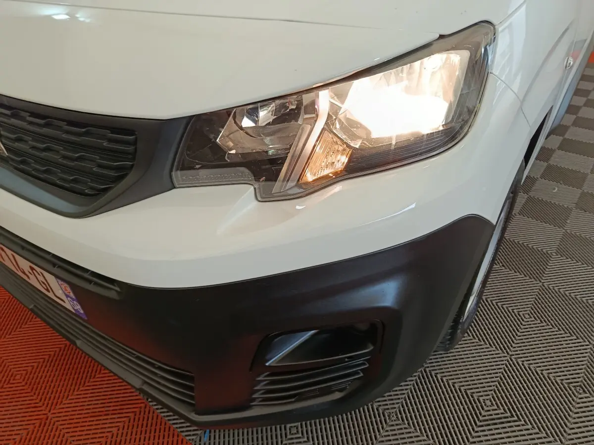 Gros plan sur l'avant droit blanc du Peugeot Partner 2021, phare allumé et pare-chocs noir mat visible.