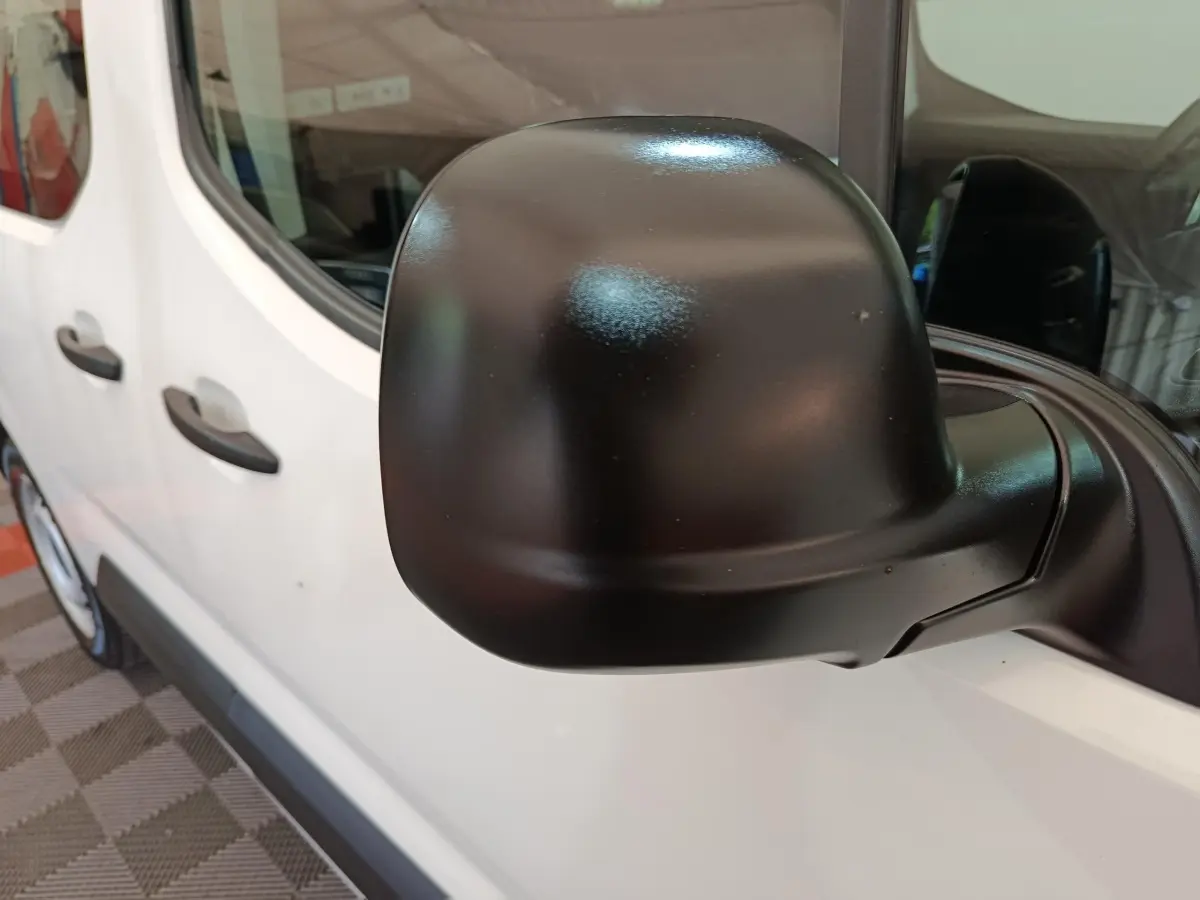 Gros plan sur le rétroviseur noir côté conducteur du Peugeot Partner blanc, vue latérale partielle du véhicule.