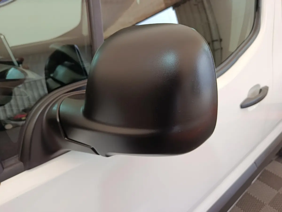 Gros plan sur le rétroviseur noir côté conducteur du Peugeot Partner blanc, avec porte et poignée visibles en arrière-plan.