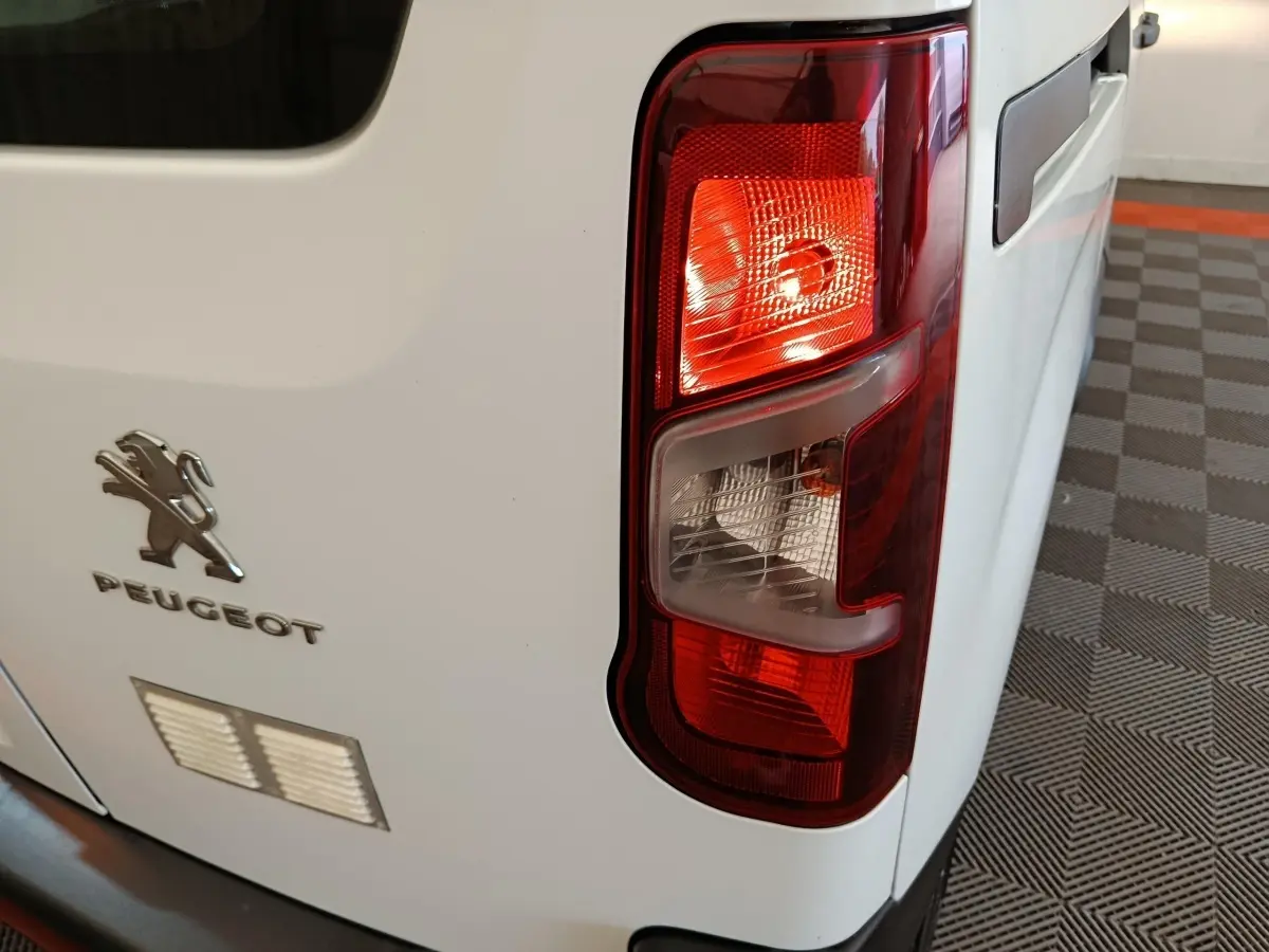 Gros plan sur le feu arrière droit d’un Peugeot Partner blanc, avec logo et partie de la porte arrière visible.
