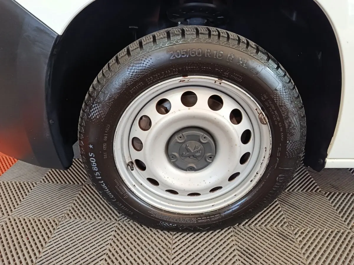 Gros plan sur la roue avant droite en jante acier du Peugeot Partner blanc, avec logo Peugeot au centre.