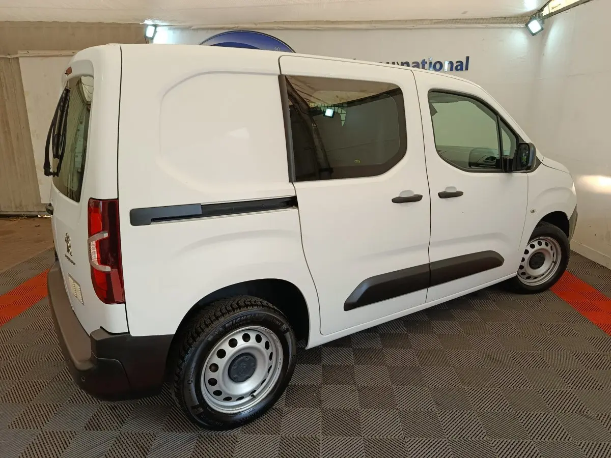 Peugeot Partner blanc vue de profil droit en intérieur, avec vitres teintées et jantes acier simples.