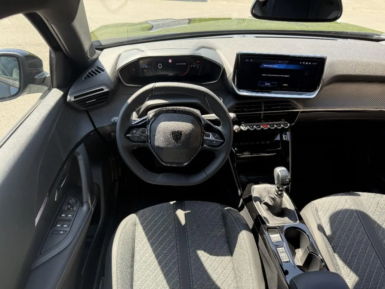 Vue intérieure avant du Peugeot 2008 2025 essence noir perla, volant compact et levier de vitesse manuel visibles.