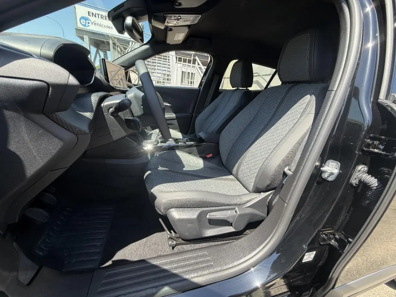 Vue intérieure côté conducteur du Peugeot 2008 noir perla 2025, montrant les sièges tissu et le tableau de bord moderne.