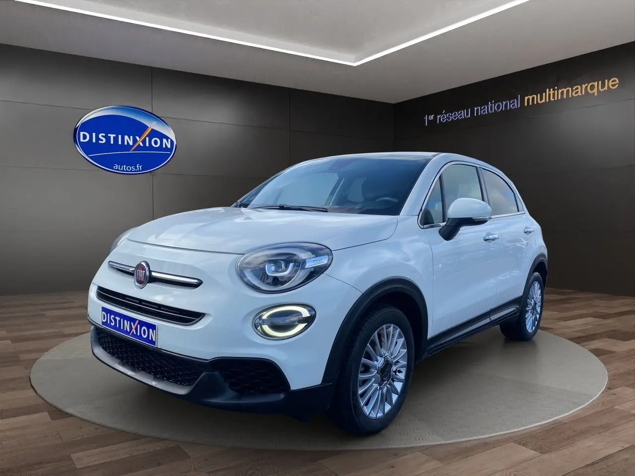 Vue 3/4 avant d'une FIAT 500X blanche avec jantes alliage et éclairage LED circulaire allumé.